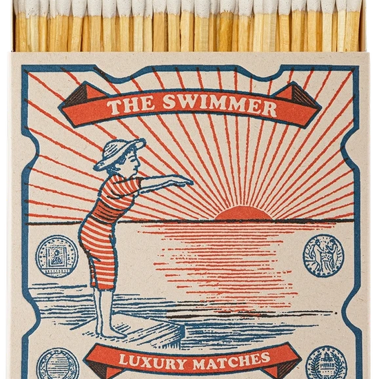 Caja de cerillas cuadrada con ilustración vintage de una mujer con bañador de rayas rojas y blancas saltando al mar, con cerillas largas de madera y punta blanca.