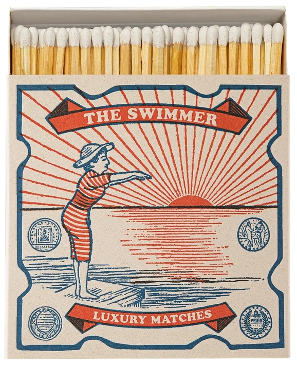 Caja de cerillas cuadrada con ilustración vintage de una mujer con bañador de rayas rojas y blancas saltando al mar, con cerillas largas de madera y punta blanca.