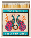 Caja de cerillas cuadrada con ilustración de dos pavos reales en azul y rosa sobre fondo crema, conteniendo cerillas largas de madera natural y punta blanca.