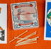 Caja de cerillas cuadrada con ilustración vintage de una mujer con bañador de rayas rojas y blancas saltando al mar, con cerillas largas de madera y punta blanca.