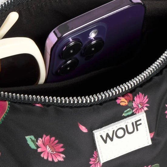 Bolso de hombro con estampado floral colorido sobre fondo oscuro, silueta suave y relajada, con correa ajustable negra y etiqueta de cuero reciclado de Wouf.