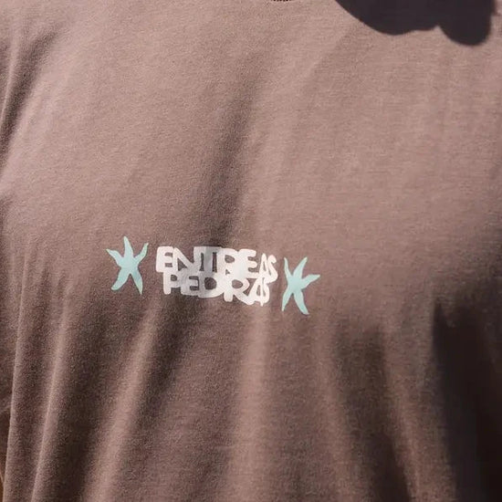 Camiseta de manga corta de corte holgado en color marrón con diseño gráfico "Entre as Pedras", confeccionada en algodón orgánico de la marca NWHR.