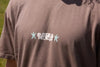 Camiseta de manga corta de corte holgado en color marrón con diseño gráfico "Entre as Pedras", confeccionada en algodón orgánico de la marca NWHR.