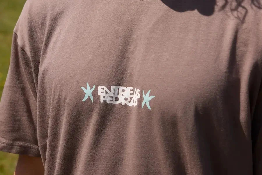 Camiseta de manga corta de corte holgado en color marrón con diseño gráfico "Entre as Pedras", confeccionada en algodón orgánico de la marca NWHR.