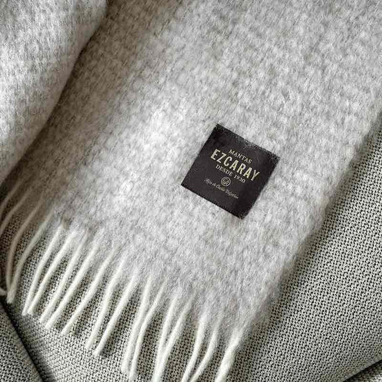 Manta de sofá de mohair en color beige crema con textura voluminosa de pelo suave, terminada con flecos y fabricada de forma artesanal en Ezcaray.
