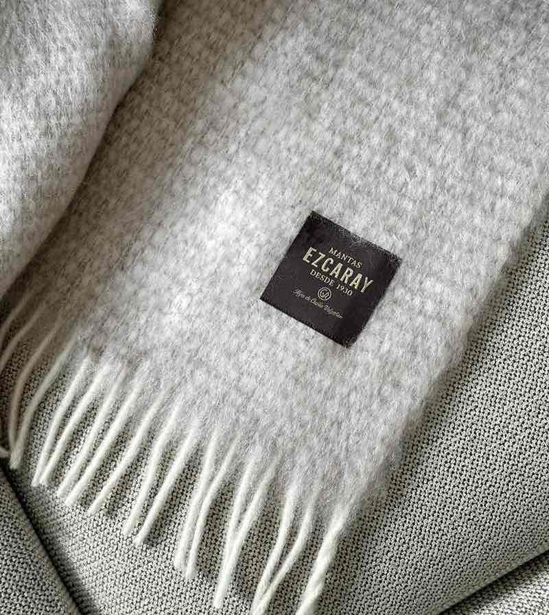 Manta de sofá de mohair en color beige crema con textura voluminosa de pelo suave, terminada con flecos y fabricada de forma artesanal en Ezcaray.