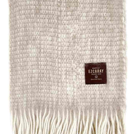 Manta de sofá de mohair en color beige crema con textura voluminosa de pelo suave, terminada con flecos y fabricada de forma artesanal en Ezcaray.
