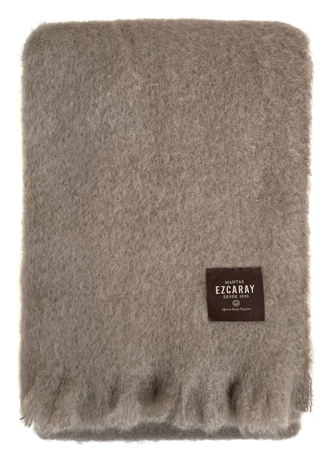 Manta de sofá de color topo con textura de mohair brillante y esponjosa, terminada en flecos manuales y fabricada mediante técnicas tradicionales en Ezcaray.