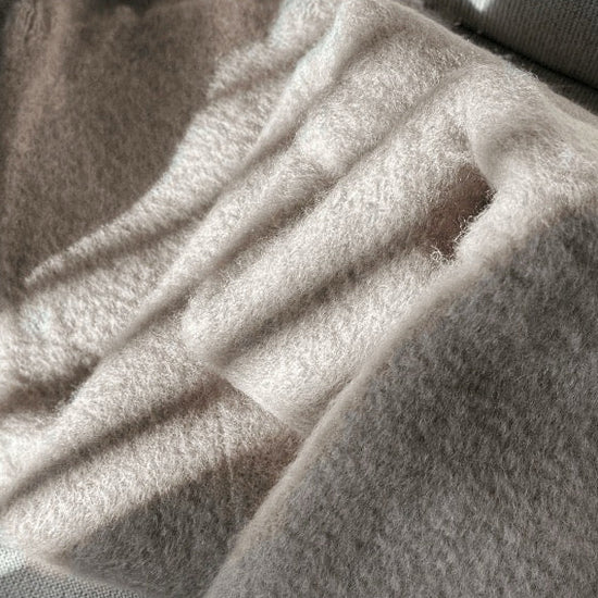 Manta de sofá de color topo con textura de mohair brillante y esponjosa, terminada en flecos manuales y fabricada mediante técnicas tradicionales en Ezcaray.