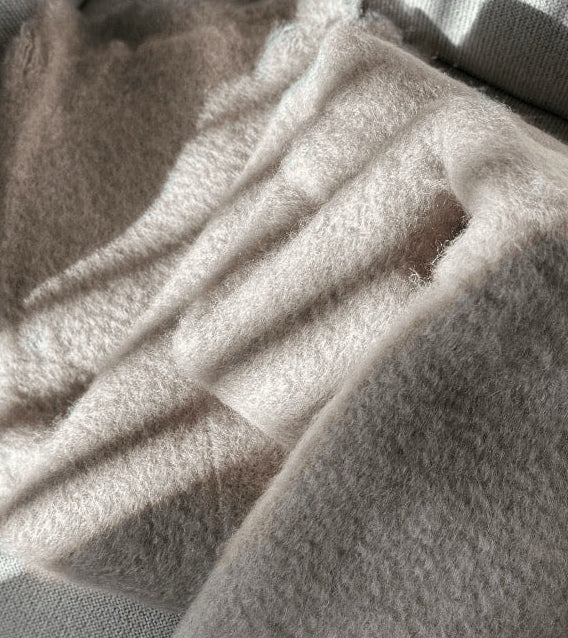 Manta de sofá de color topo con textura de mohair brillante y esponjosa, terminada en flecos manuales y fabricada mediante técnicas tradicionales en Ezcaray.