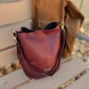Bolso tipo bombonera de piel lisa color burdeos con asa corta de mano y bandolera ajustable, cierre de imán y fabricación artesanal española de The Code.