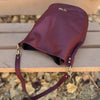 Bolso tipo bombonera de piel lisa color burdeos con asa corta de mano y bandolera ajustable, cierre de imán y fabricación artesanal española de The Code.