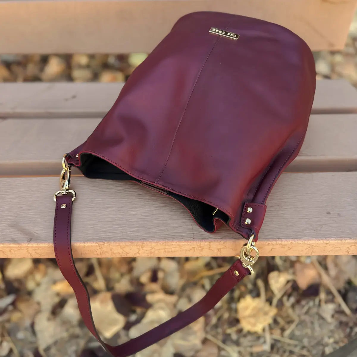 Bolso tipo bombonera de piel lisa color burdeos con asa corta de mano y bandolera ajustable, cierre de imán y fabricación artesanal española de The Code.