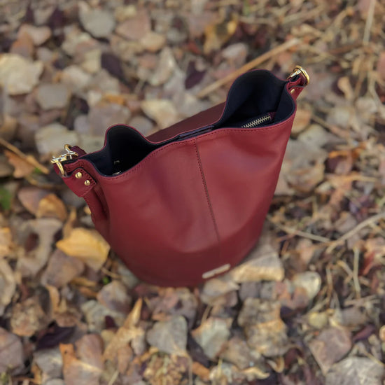 Bolso tipo bombonera de piel lisa color burdeos con asa corta de mano y bandolera ajustable, cierre de imán y fabricación artesanal española de The Code.
