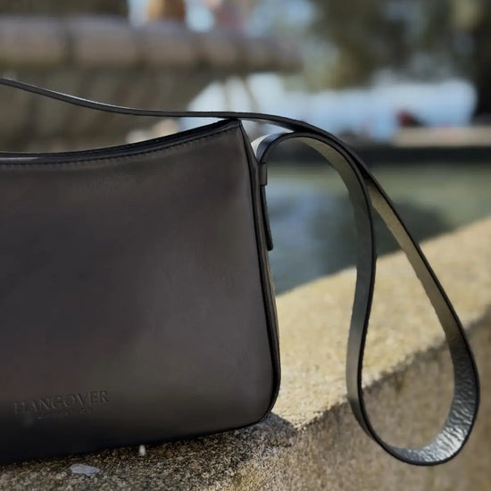 Bolso pequeño estructurado de piel napa negra con asa ajustable y diseño minimalista de la marca Hangover of Fashion, fabricado artesanalmente en España.