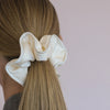 Coletero tipo scrunchie gigante de color blanco roto con capas de tela en forma de pétalos de flor anémona de la marca danesa By Stær.
