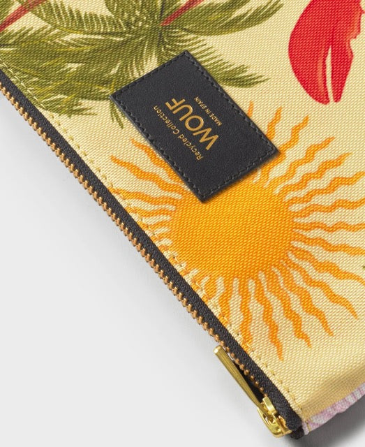 Neceser plano con estampado tropical de aves y flores exóticas sobre fondo oscuro, con cierre de cremallera dorada y etiqueta de cuero reciclado de Wouf.