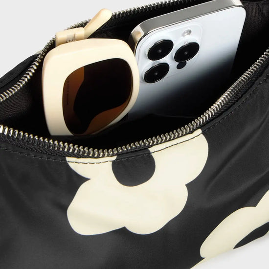 Bolso de hombro con estampado de margaritas blancas sobre fondo oscuro, logo metálico frontal, cremallera superior y correa ajustable, modelo Night Daisy de Wouf.