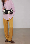 Bolso de hombro con estampado de margaritas blancas sobre fondo oscuro, logo metálico frontal, cremallera superior y correa ajustable, modelo Night Daisy de Wouf.
