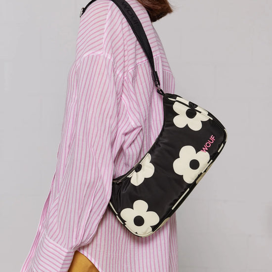 Bolso de hombro con estampado de margaritas blancas sobre fondo oscuro, logo metálico frontal, cremallera superior y correa ajustable, modelo Night Daisy de Wouf.