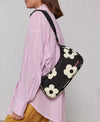 Bolso de hombro con estampado de margaritas blancas sobre fondo oscuro, logo metálico frontal, cremallera superior y correa ajustable, modelo Night Daisy de Wouf.