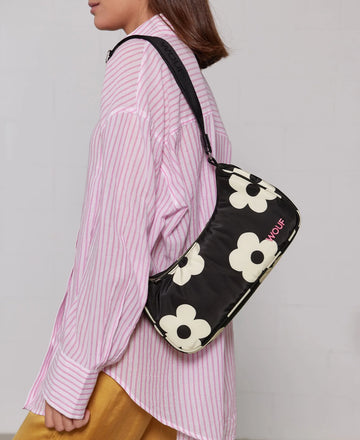 Bolso de hombro con estampado de margaritas blancas sobre fondo oscuro, logo metálico frontal, cremallera superior y correa ajustable, modelo Night Daisy de Wouf.