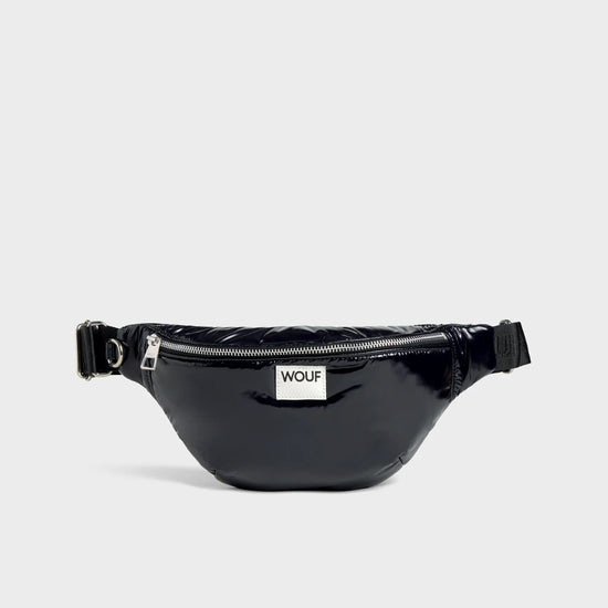 Riñonera negra con acabado brillante de la colección Nuit de Wouf, con correa ajustable, cremallera superior y etiqueta de cuero reciclado con logo frontal.
