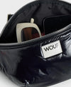 Riñonera negra con acabado brillante de la colección Nuit de Wouf, con correa ajustable, cremallera superior y etiqueta de cuero reciclado con logo frontal.