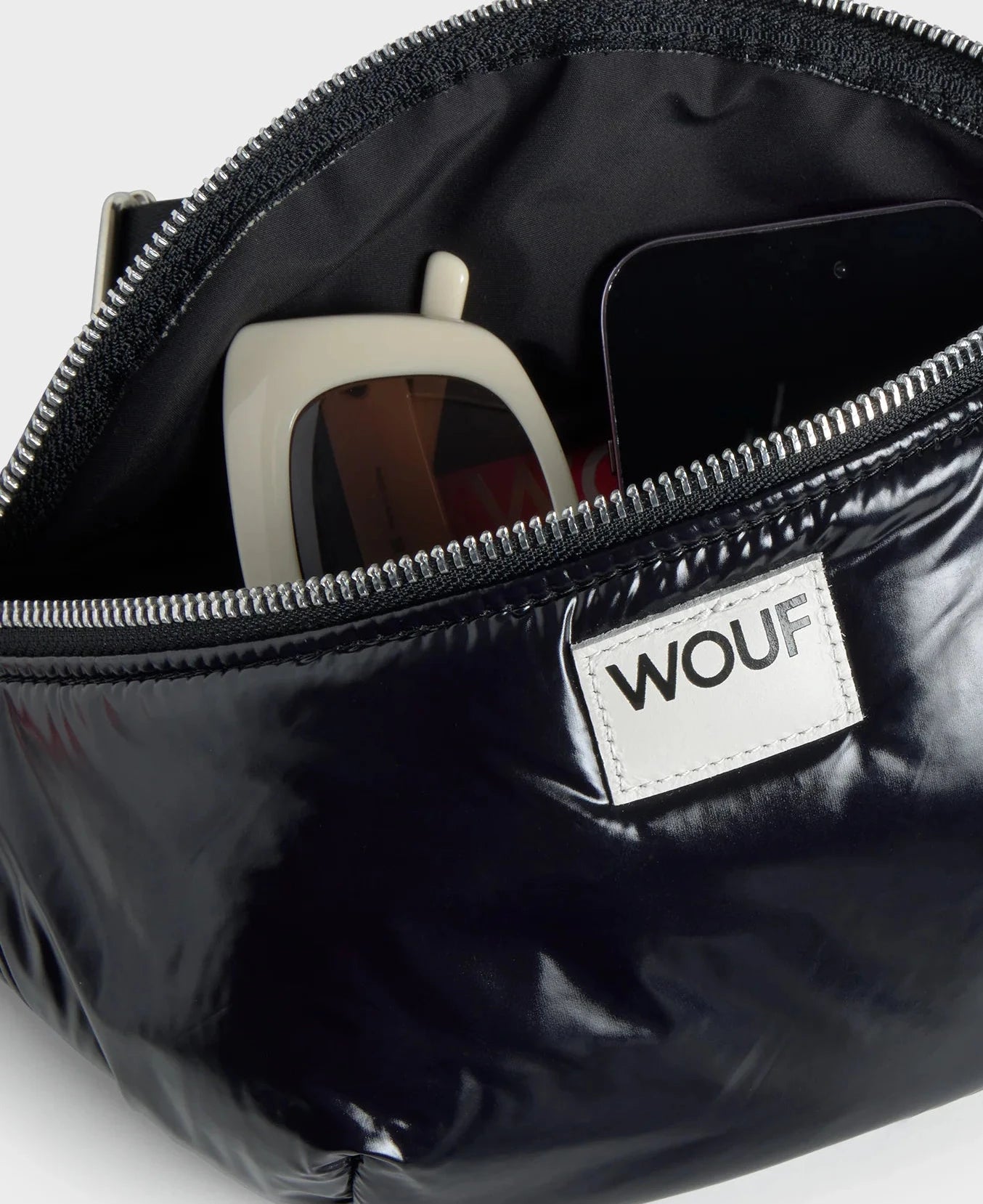 Riñonera negra con acabado brillante de la colección Nuit de Wouf, con correa ajustable, cremallera superior y etiqueta de cuero reciclado con logo frontal.