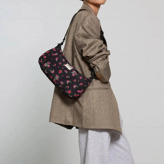 Bolso de hombro con estampado floral colorido sobre fondo oscuro, silueta suave y relajada, con correa ajustable negra y etiqueta de cuero reciclado de Wouf.
