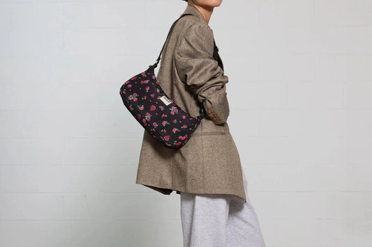 Bolso de hombro con estampado floral colorido sobre fondo oscuro, silueta suave y relajada, con correa ajustable negra y etiqueta de cuero reciclado de Wouf.
