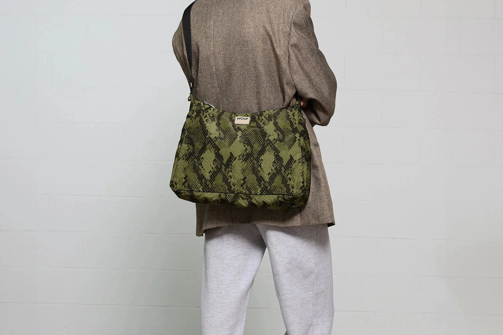 Bolso tipo hobo con estampado de piel de serpiente en tonos oscuros, con silueta curva, correa ajustable negra y detalle de etiqueta de cuero de Wouf.