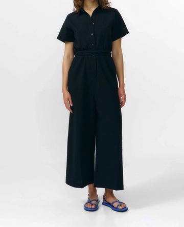 Mono largo de color negro con manga corta, cuello de camisa y pernera ancha, que incluye un cinturón a juego y botones naturales en la parte frontal.
