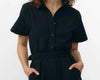 Mono largo de color negro con manga corta, cuello de camisa y pernera ancha, que incluye un cinturón a juego y botones naturales en la parte frontal.
