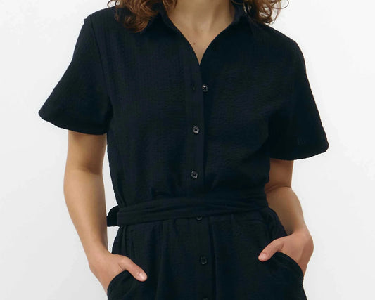 Mono largo de color negro con manga corta, cuello de camisa y pernera ancha, que incluye un cinturón a juego y botones naturales en la parte frontal.