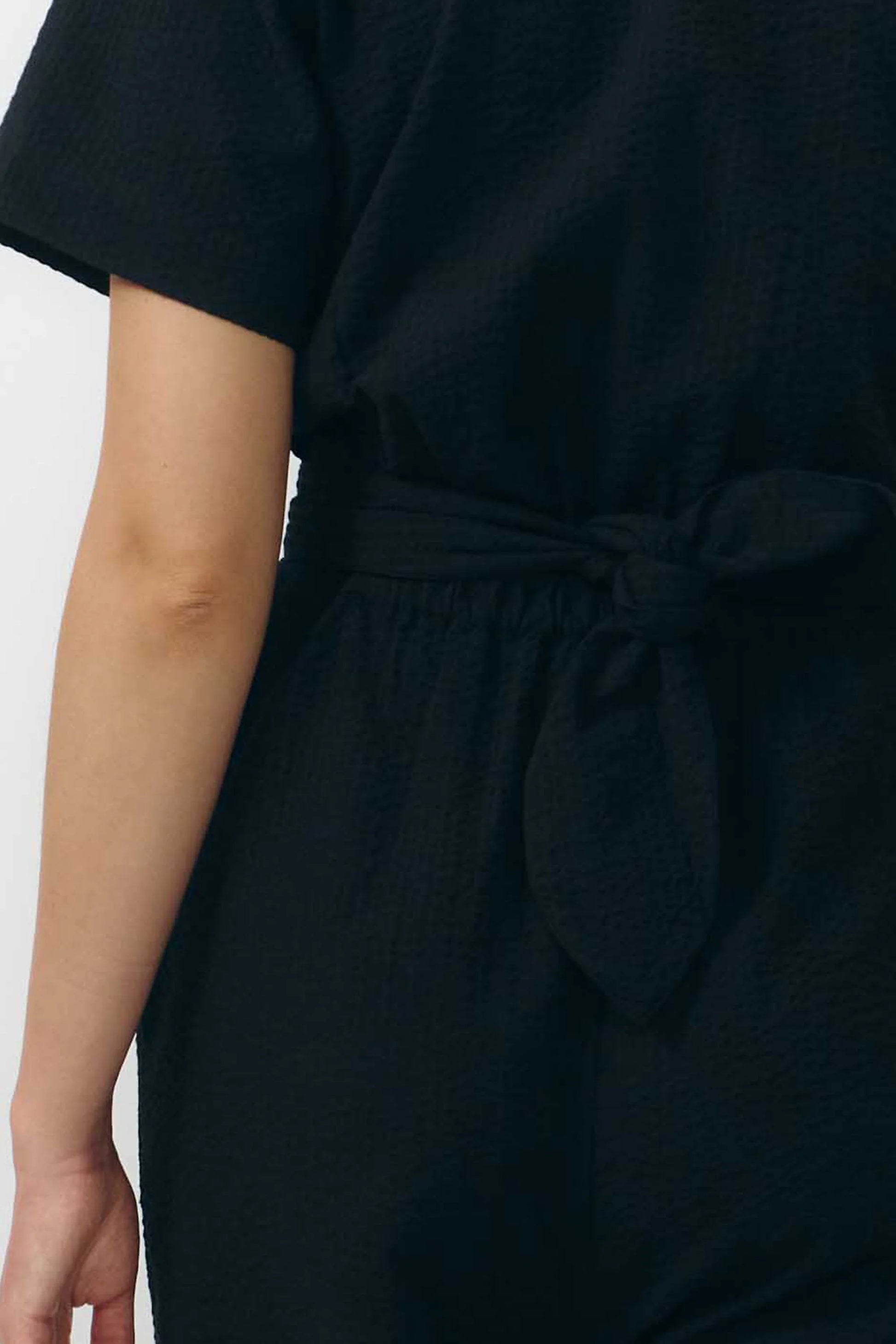 Mono largo de color negro con manga corta, cuello de camisa y pernera ancha, que incluye un cinturón a juego y botones naturales en la parte frontal.
