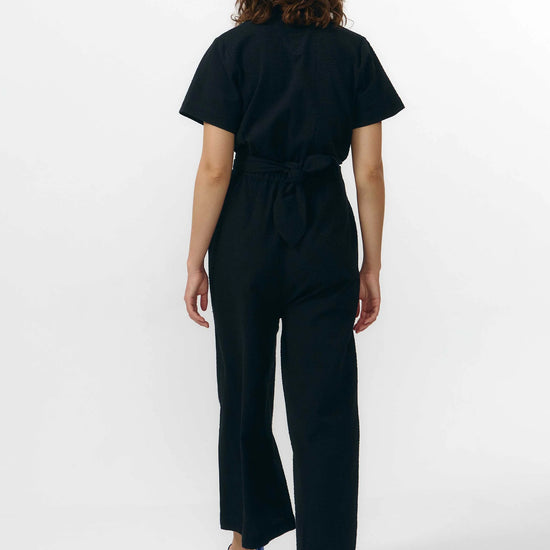 Mono largo de color negro con manga corta, cuello de camisa y pernera ancha, que incluye un cinturón a juego y botones naturales en la parte frontal.