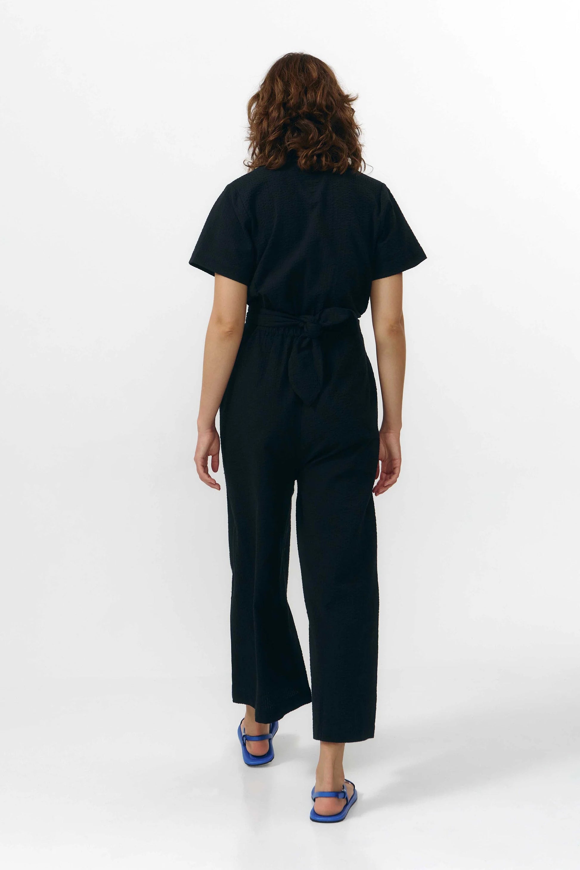 Mono largo de color negro con manga corta, cuello de camisa y pernera ancha, que incluye un cinturón a juego y botones naturales en la parte frontal.