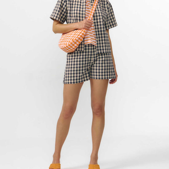 Camisa de manga corta con estampado de cuadros en tonos grises, cuello de solapa, dos bolsillos frontales cuadrados y cierre de botones naturales de corozo.
