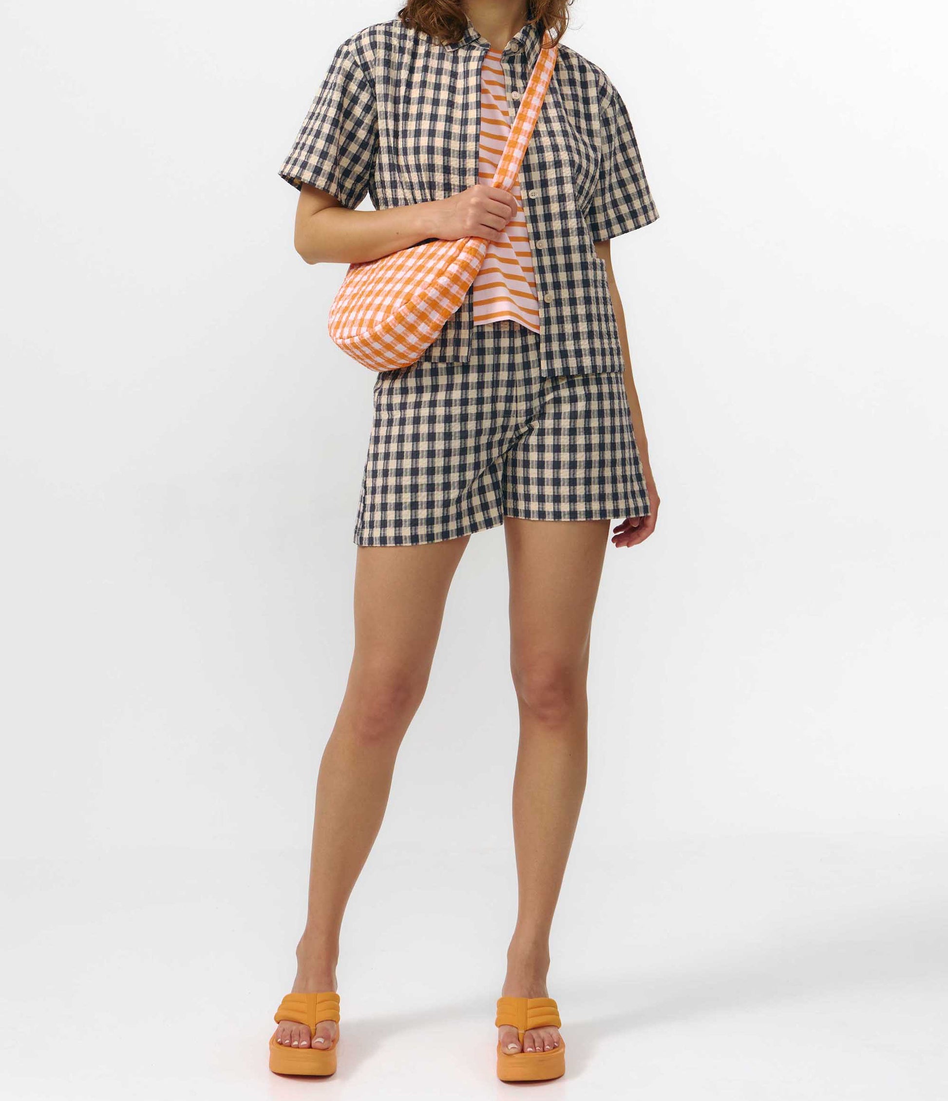 Camisa de manga corta con estampado de cuadros en tonos grises, cuello de solapa, dos bolsillos frontales cuadrados y cierre de botones naturales de corozo.