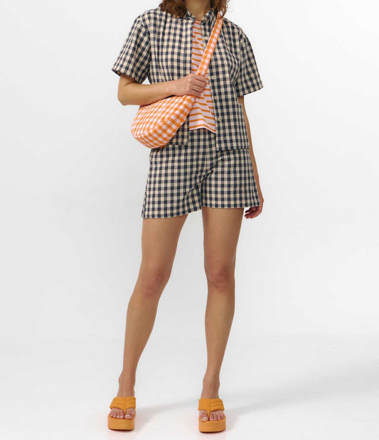 Camisa de manga corta con estampado de cuadros en tonos grises, cuello de solapa, dos bolsillos frontales cuadrados y cierre de botones naturales de corozo.