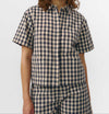 Camisa de manga corta con estampado de cuadros en tonos grises, cuello de solapa, dos bolsillos frontales cuadrados y cierre de botones naturales de corozo.