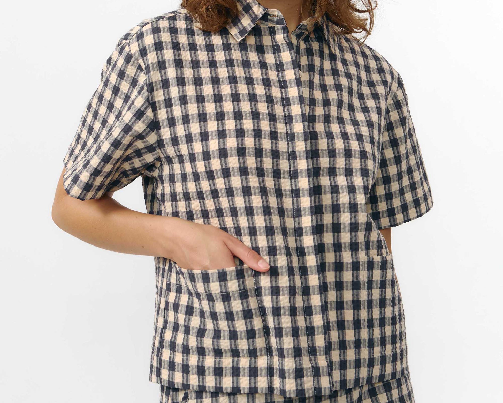 Camisa de manga corta con estampado de cuadros en tonos grises, cuello de solapa, dos bolsillos frontales cuadrados y cierre de botones naturales de corozo.