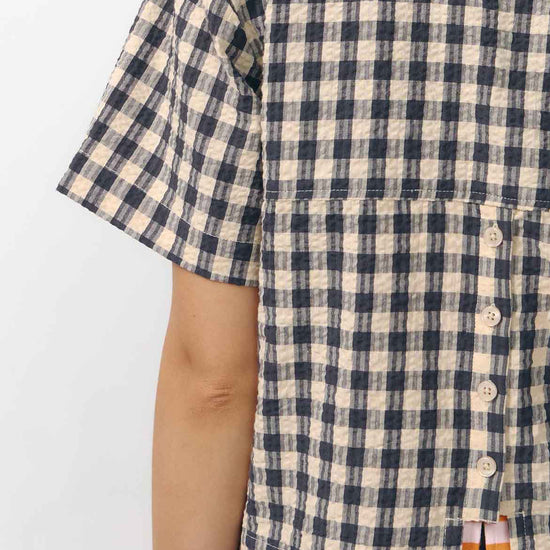 Camisa de manga corta con estampado de cuadros en tonos grises, cuello de solapa, dos bolsillos frontales cuadrados y cierre de botones naturales de corozo.