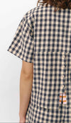 Camisa de manga corta con estampado de cuadros en tonos grises, cuello de solapa, dos bolsillos frontales cuadrados y cierre de botones naturales de corozo.