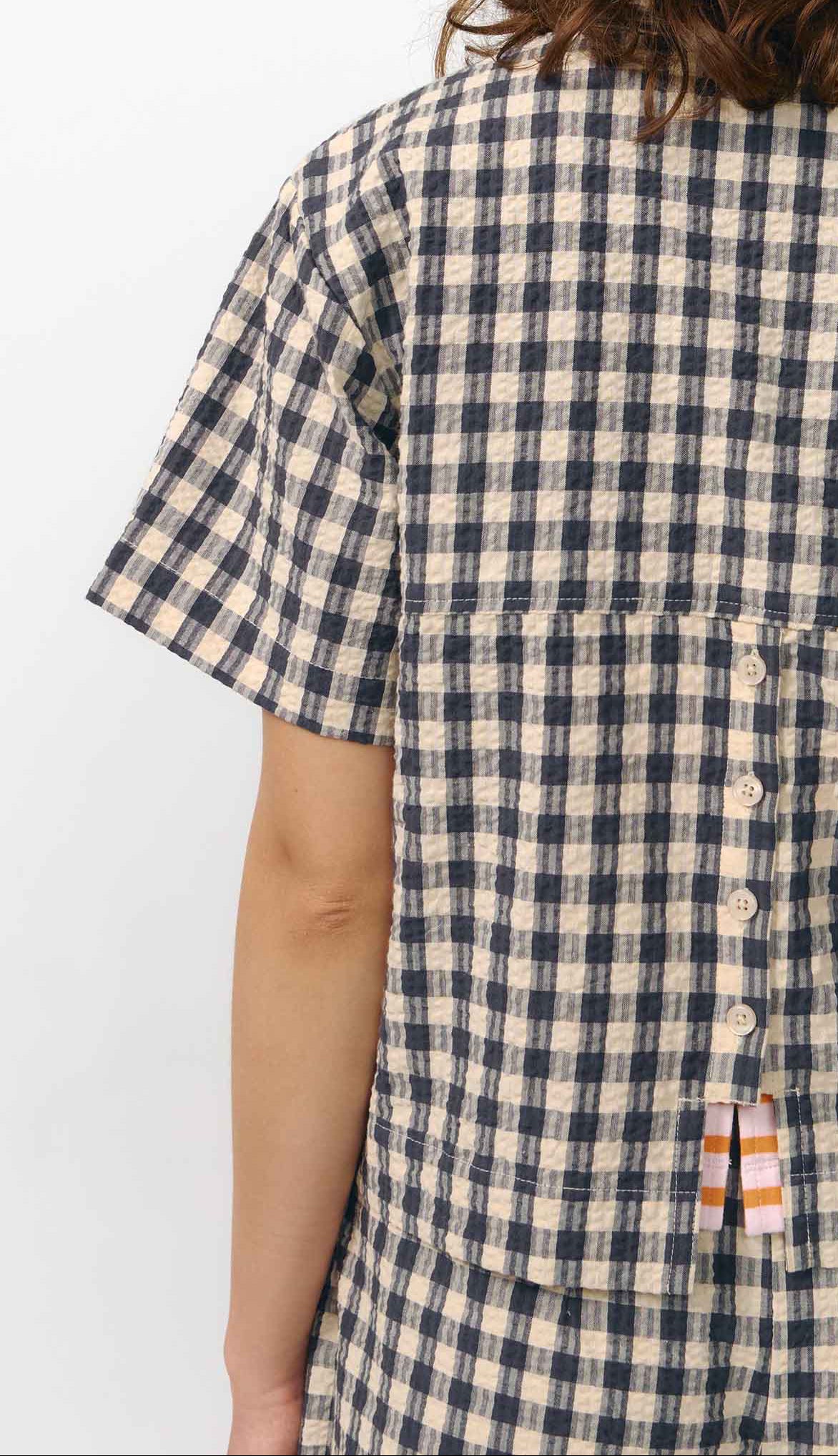 Camisa de manga corta con estampado de cuadros en tonos grises, cuello de solapa, dos bolsillos frontales cuadrados y cierre de botones naturales de corozo.