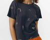 Top de algodón orgánico gris oscuro de manga corta con bordados decorativos, cuello redondo delantero y escote en pico en la espalda de la marca Suite13 Lab.