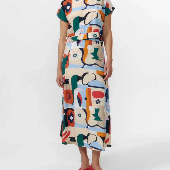 Falda midi de tejido fluido con estampado artístico de barcos y motivos marinos en azul sobre fondo crema, con una abertura lateral en el bajo.