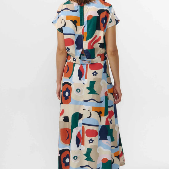 Falda midi de tejido fluido con estampado artístico de barcos y motivos marinos en azul sobre fondo crema, con una abertura lateral en el bajo.