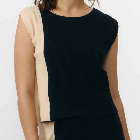 Top ajustado sin mangas en color negro con textura de punto waffle, cuello redondo y detalle de cierre trasero con un pequeño botón de madera natural.